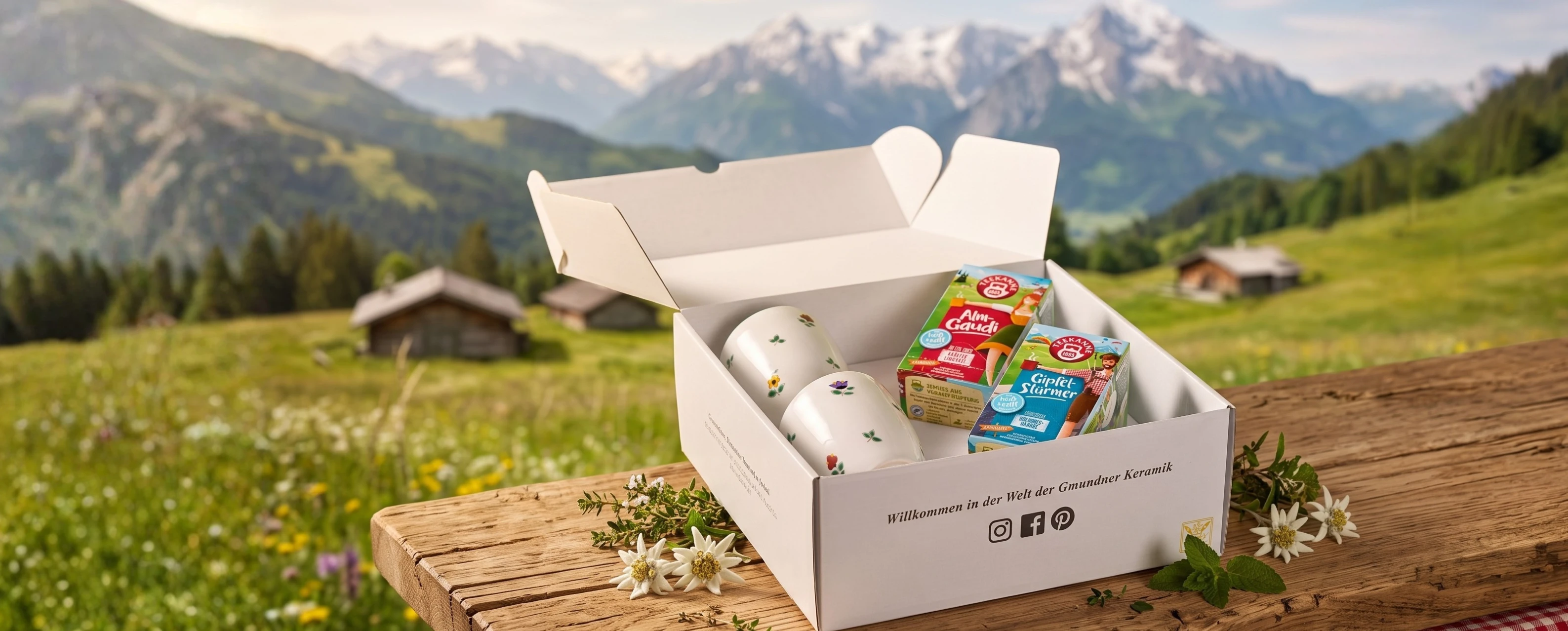 Weiße Schachtel mit Tassen und Milchprodukten auf einem Holztisch, im Hintergrund eine Alpenlandschaft und Berge.
