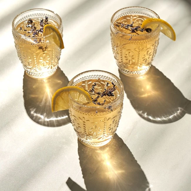 Drei dekorative Gläser mit Zitronen-Lavendel-Getränken werfen komplizierte Schatten und Reflexionen auf eine sonnige Oberfläche.