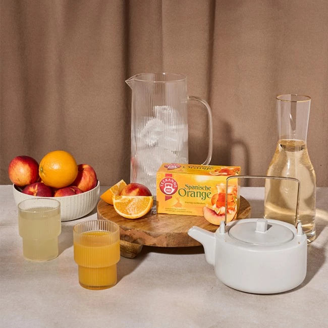 Ein Frühstückstisch mit Orangen, Saft, spanischem Orangentee, Eiswasserkrug und Teekanne.