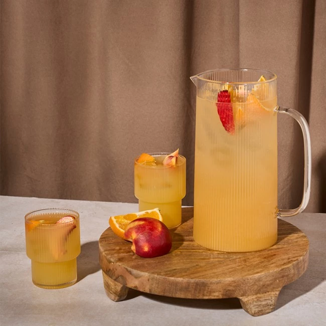 Krug und Gläser Orangensaft mit Fruchtscheiben auf einem Holzbrett, Pfirsich und Orange in der Nähe.