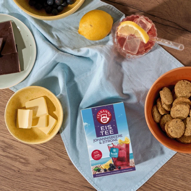 Teekanne-Eisteebox auf dem Tisch mit Keksen, Schokolade, Butter, Trauben, Zitrone und Eistee.