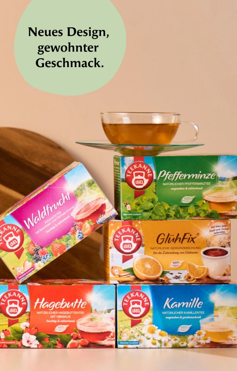 Gestapelte bunte Teedosen mit gläsernen Teetassen, rundem Schild von Neues Design und Schneidebrett dahinter.