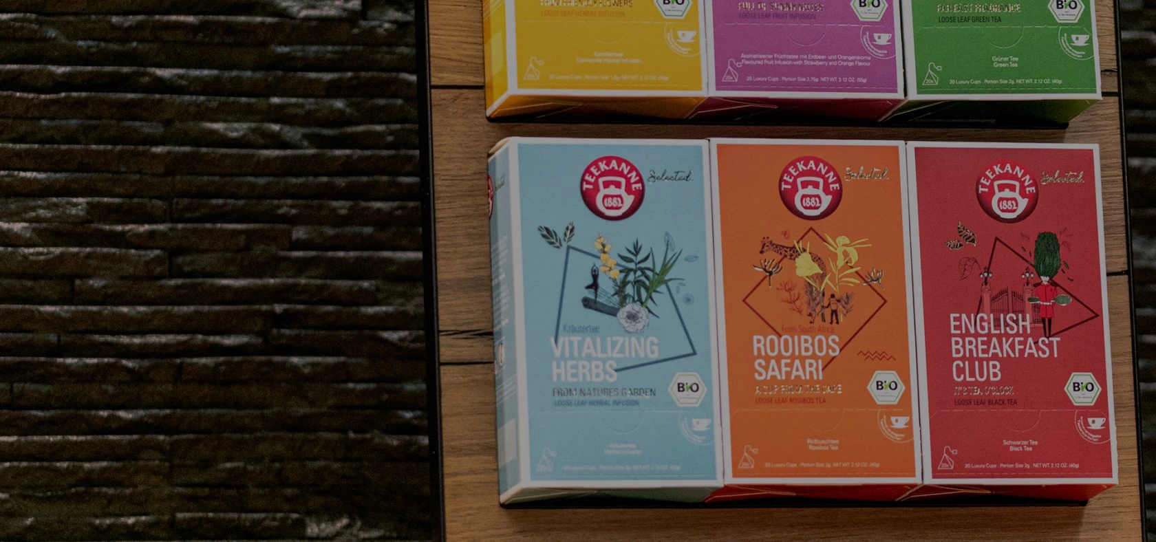 Drei Teekannen-Teedosen auf Holz, links teilweise sichtbarer schwarzer strukturierter Hintergrund.