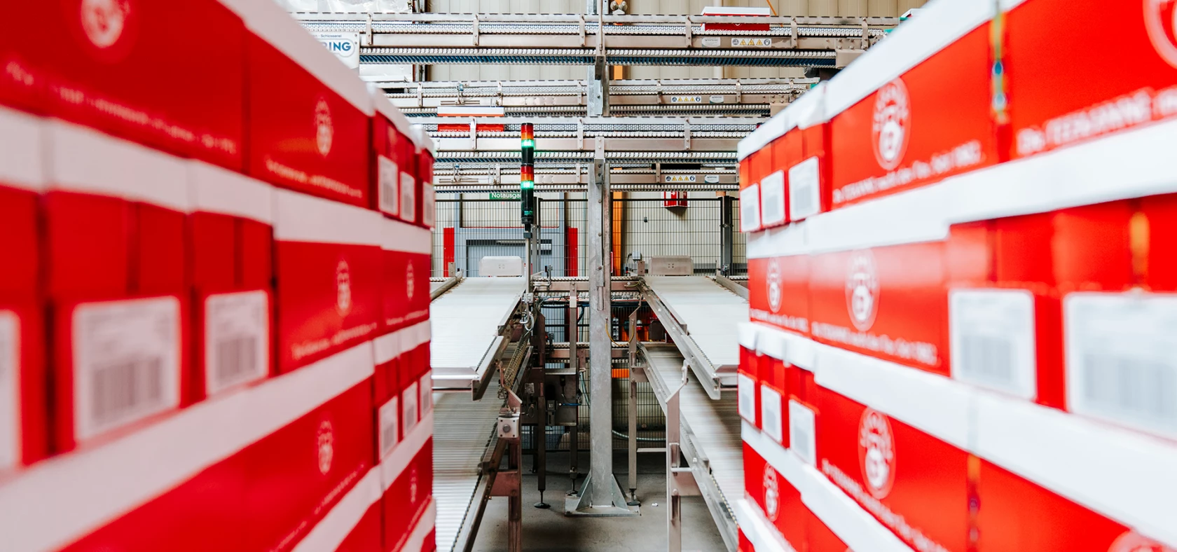 In einem modernen Lagerhaus stapeln sich rote und weiße Kartons auf einem Förderband.