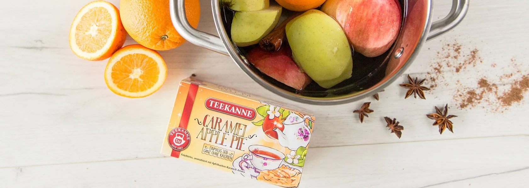 Topf mit Äpfeln, Orangen im Wasser; geschnittene Orangen, Teedose, Sternanis und Zimt in der Nähe.