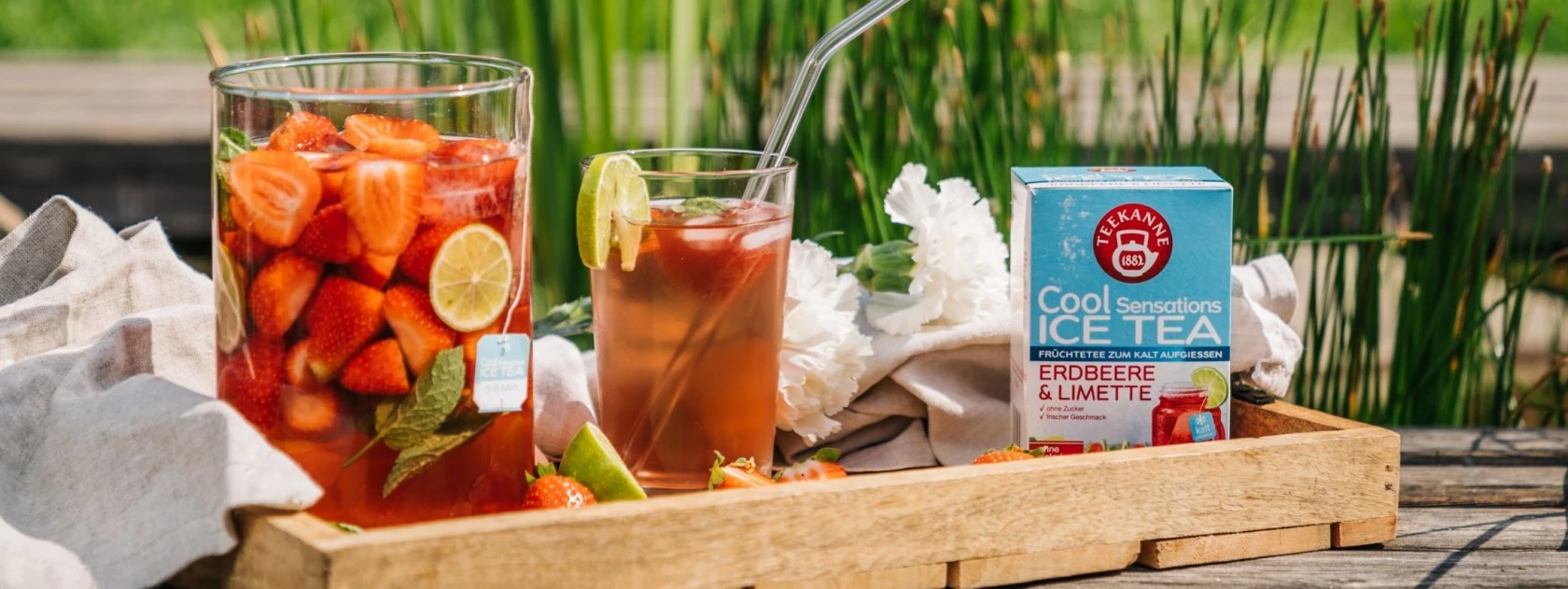 Krug und Glas Erdbeer-Limetten-Eistee mit Minze, Cool Sensations-Box, dahinter Grünpflanzen.