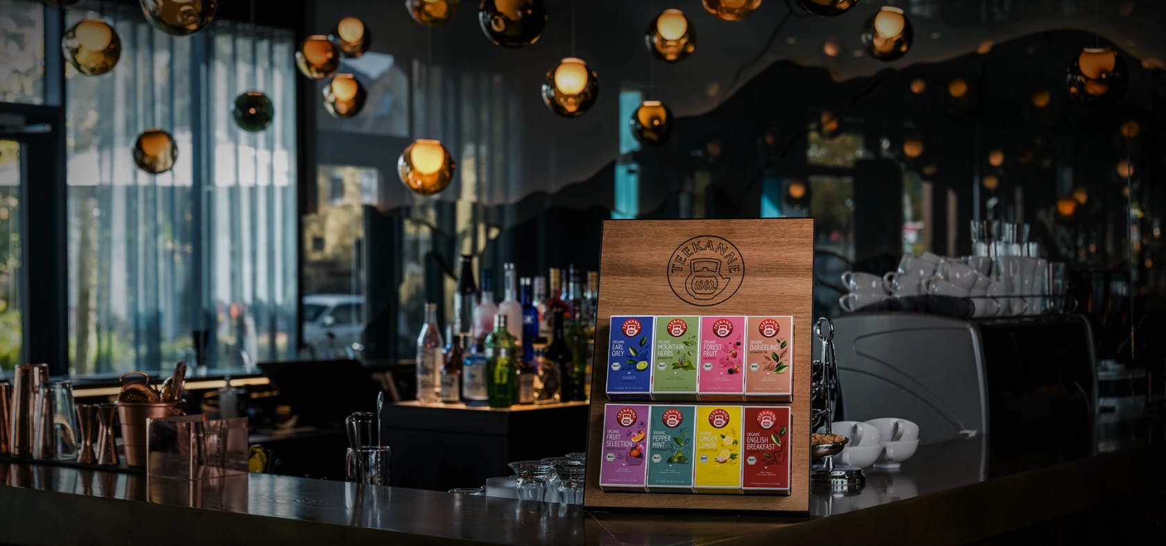 Bunte Schokoriegel auf einem Holzständer, im Hintergrund eine Bartheke, Flaschen und Hängelampen.