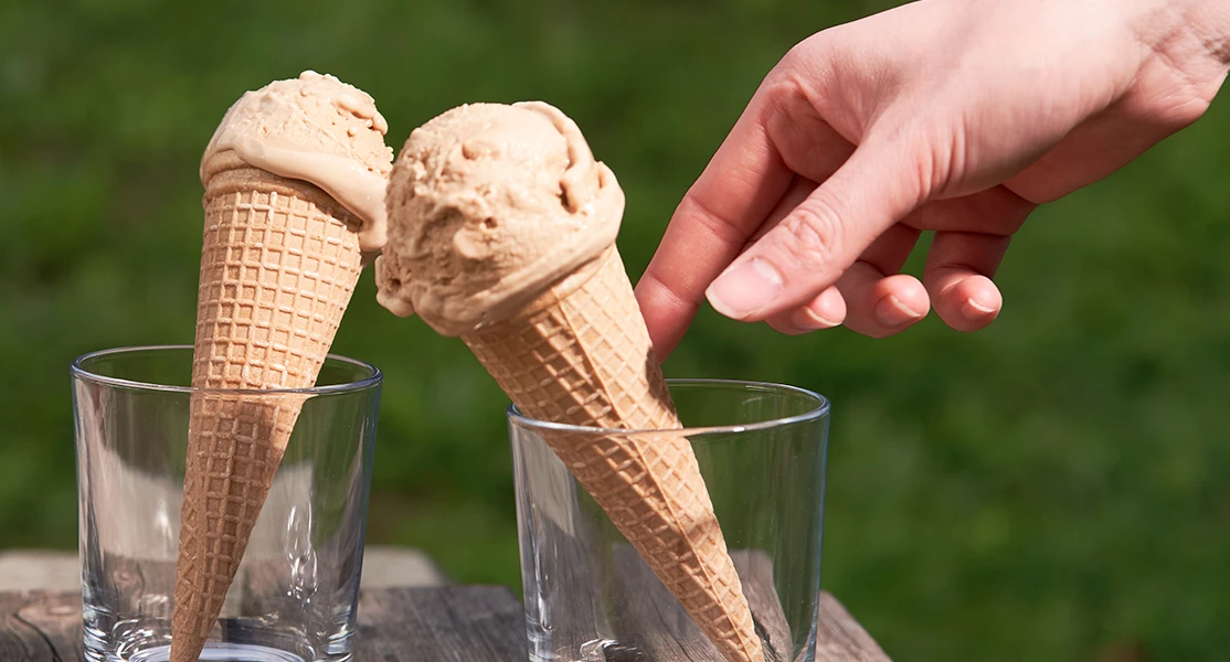 Hand nimmt Eistüte aus Glas; eine weitere Tüte und eine Schachtel English Breakfast-Tee stehen auf einer Holzoberfläche.