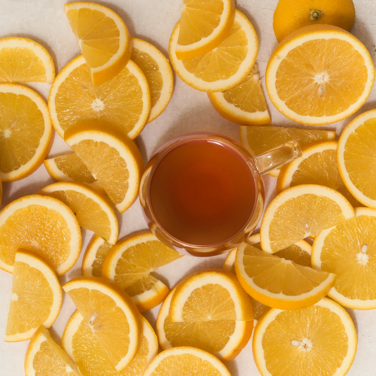 Auf einer Oberfläche steht ein Glas mit BIO Orange Ingwer, umgeben von überlappenden Scheiben frischer Orange und einer ganzen Orange in der oberen rechten Ecke, wodurch ein helles und optisch ansprechendes Arrangement entsteht.