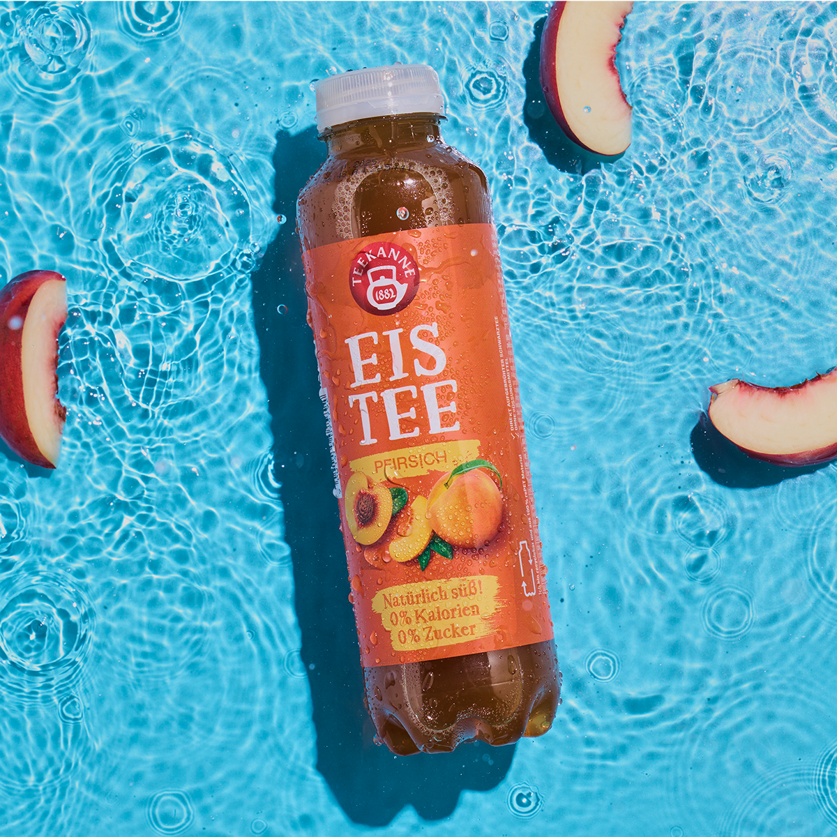 Eine Flasche Pfirsich schwimmt mit Pfirsichscheiben im klaren blauen Wasser. Das orangefarbene Etikett zeigt saftige Pfirsiche und erfrischende Wassertropfen.