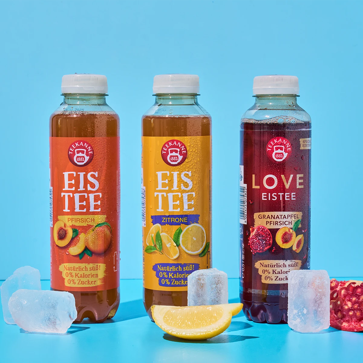 Das Eistee Probierpaket + gratis Zitrone (12l) präsentiert sich mit drei Flaschen auf blauem Hintergrund, umgeben von Eiswürfeln, einer Zitronenscheibe und einem Granatapfelstück für extra Sommer-Erfrischung.