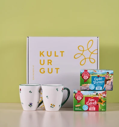 Das Landlust Geschenkset besteht aus zwei weißen Bechern mit floralem Muster, einer KULTURGUT-Schachtel sowie Gipfelstürmer- und Almgaudi-Schachteln auf hellgelber Oberfläche und ist damit ein perfektes Geschenk.